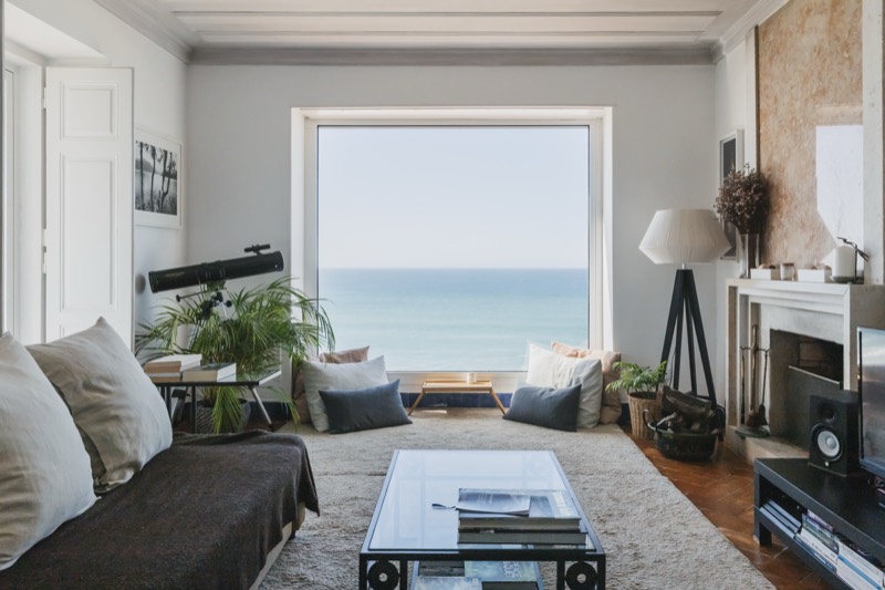 Living room with a cream sofa, stone fireplace and a picture window framing the Atlantic at golden hour